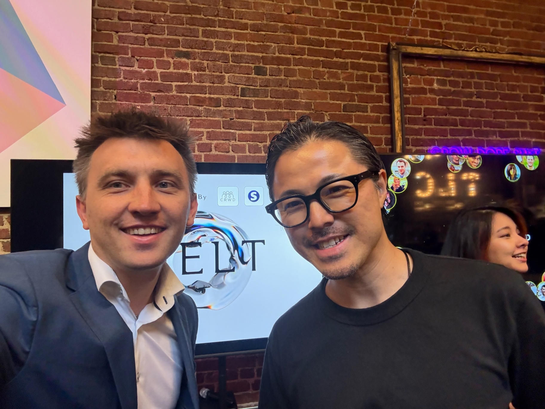 Host and a founder posing at an evening event with brick wall backdrop
